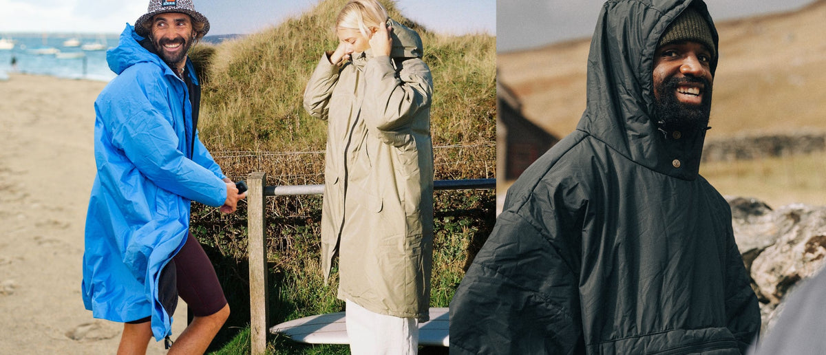 Three outdoor lifestyle shots showing people wearing hooded waterproof jackets in beach and dune settings. The left figure wears a bright blue hooded jacket, the center figure wears a light olive-beige hooded jacket, and the right figure wears a dark charcoal hooded jacket. Allweather Coat, ChangeRobe,Poncho VOITED