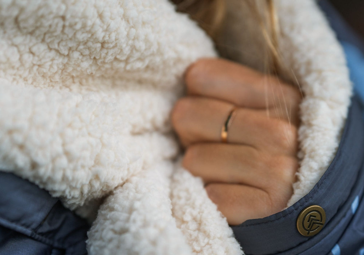 Close-up of a person's hand holding the cream sherpa fleece lining of a VOITED Cloudtouch Blanket, with the VOITED logo visible on the navy button trim.